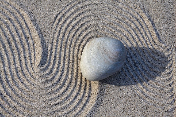 Wellen im Sand, auf denen ein einzelner Stein liegt.