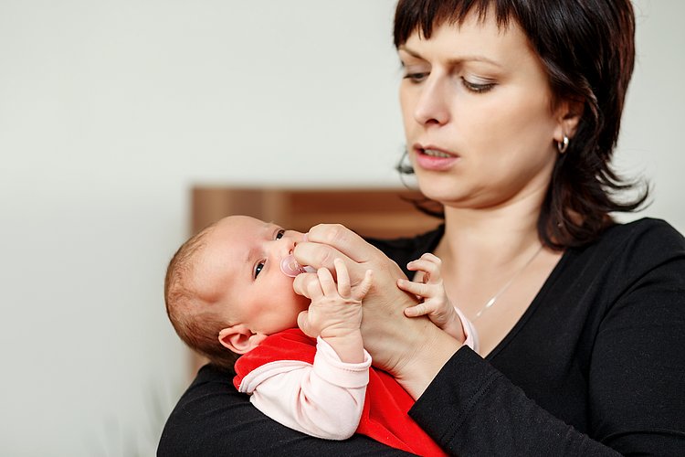 Eine Mutter hat ein Baby im Arm und versucht es zu beruhigen