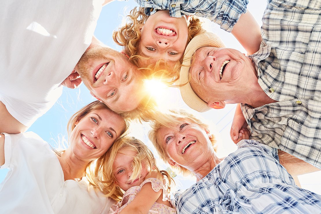 AdobeStock 256161582 6 Personen verschiedener Generationen umarmen sich Kopf an Kopf im Kreis und lachen dabei.